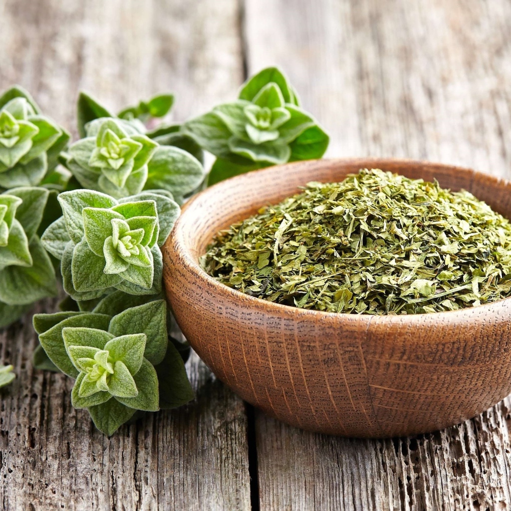 Сухая трава орегано в деревянной миске на столе 