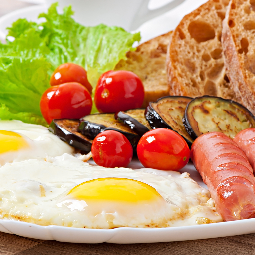 Яичница на тарелке с сосисками, овощами и хлебом