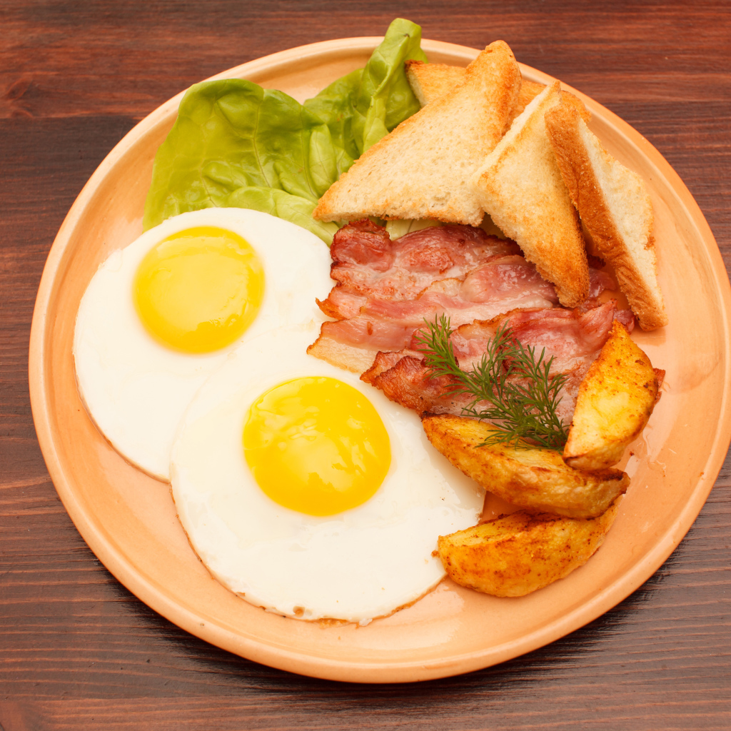 Fried eggs with bacon, french fries and croutons on the table