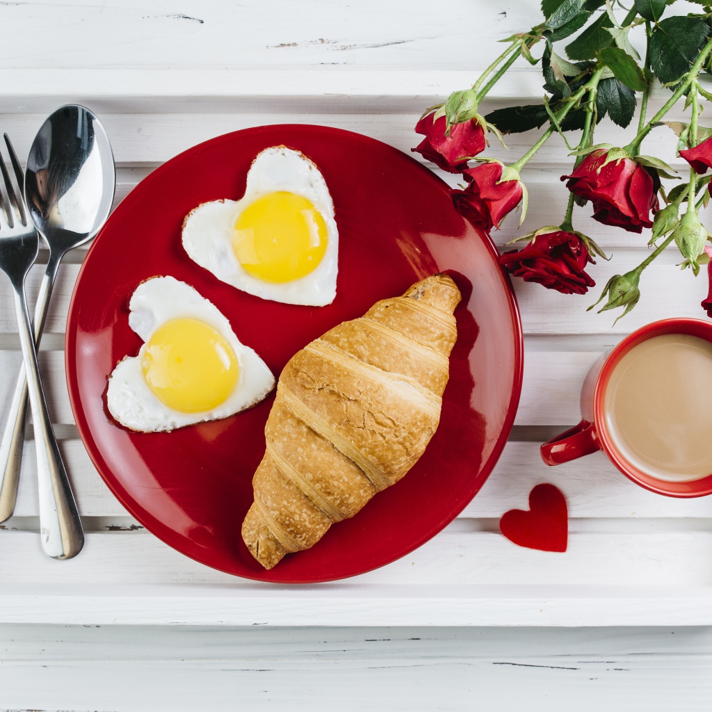 Яичница с круассаном на красной тарелке на столе букетом роз и чашкой какао