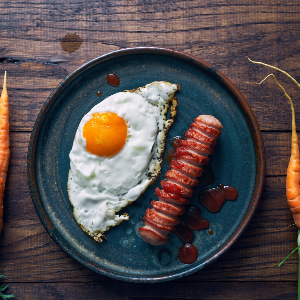 Яичница с сосиской на столе с морковью 