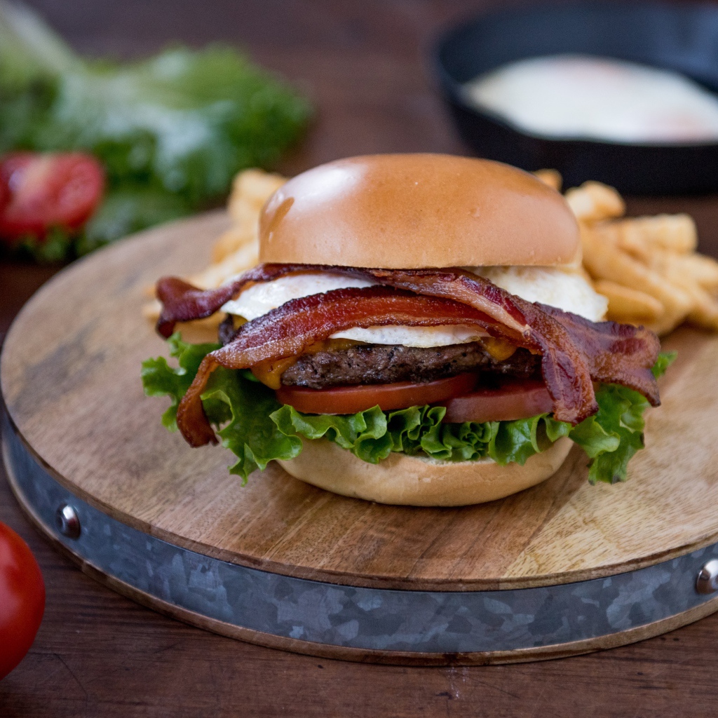 Гамбургер с беконом на столе с овощами