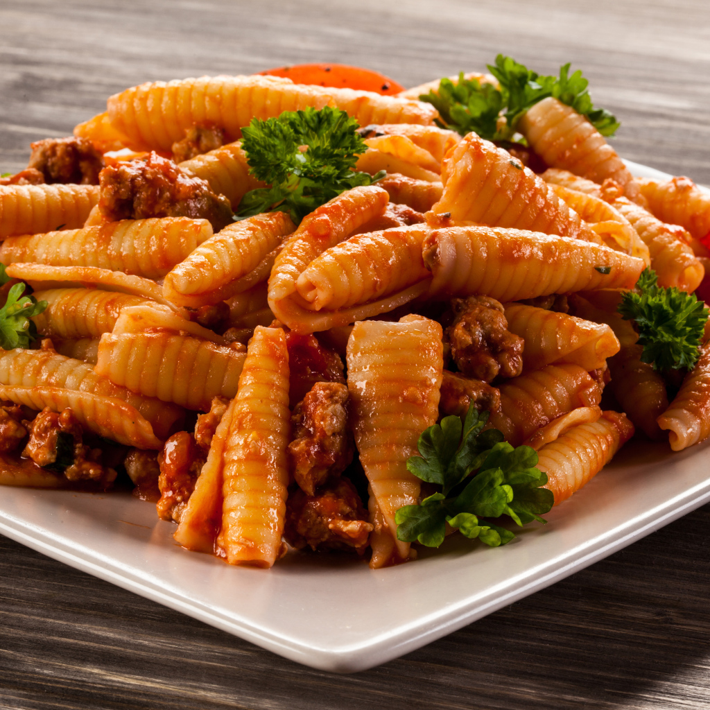 Паста с мясом, петрушкой и помидорами на белой тарелке