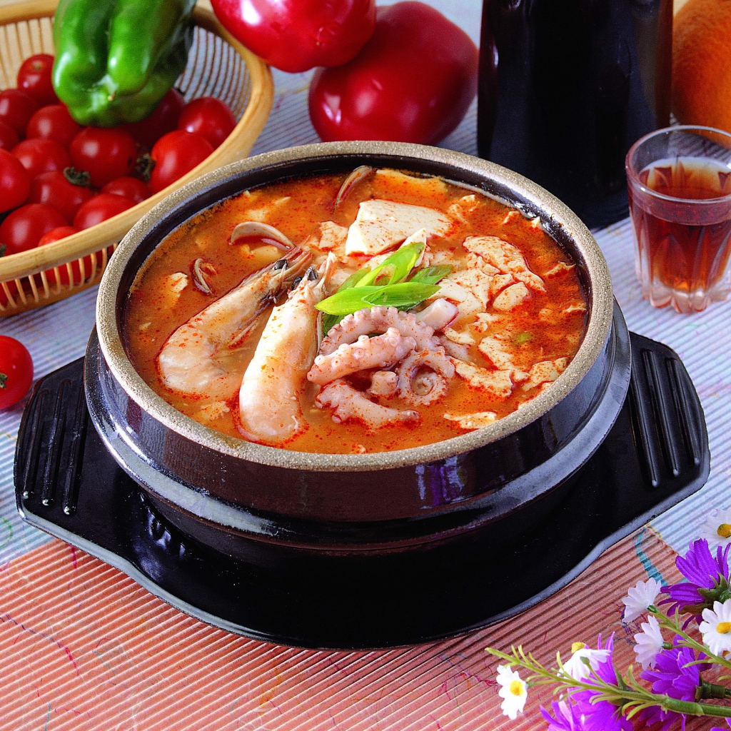 Тарелка красного супа с морепродуктами на столе с овощами 