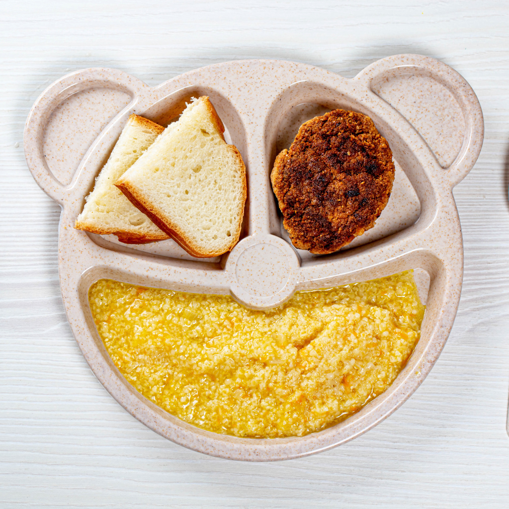 Каша на тарелке с котлетой и хлебом для ребенка