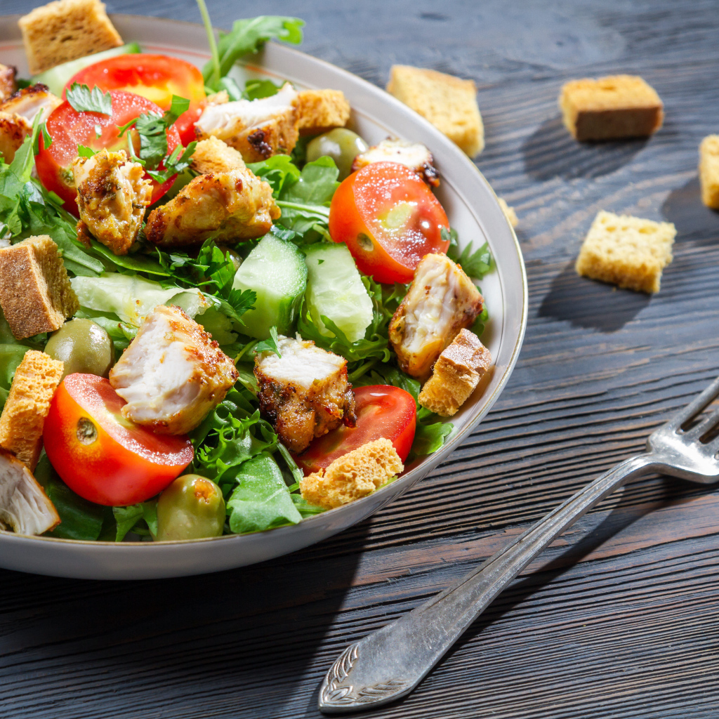 Салат с овощами, сухариками и курицей и на столе с вилкой