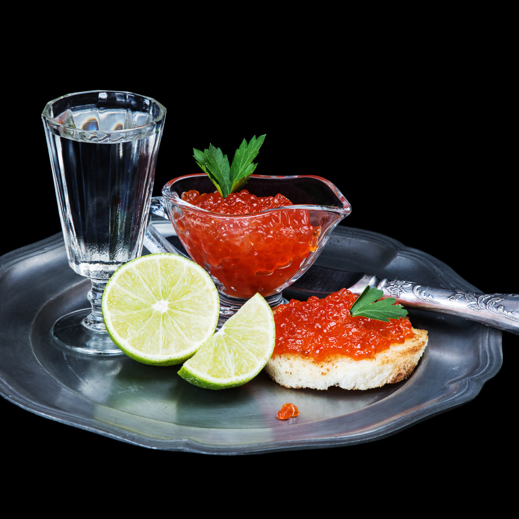 Бутерброды с красной икрой на подносе с рюмкой водки и лаймом