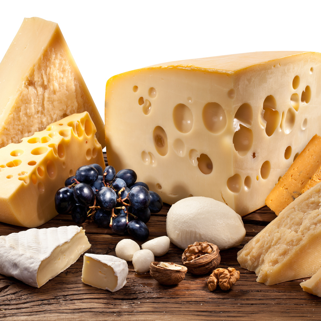 Куски сыра на деревянном столе с виноградом и грецким орехом