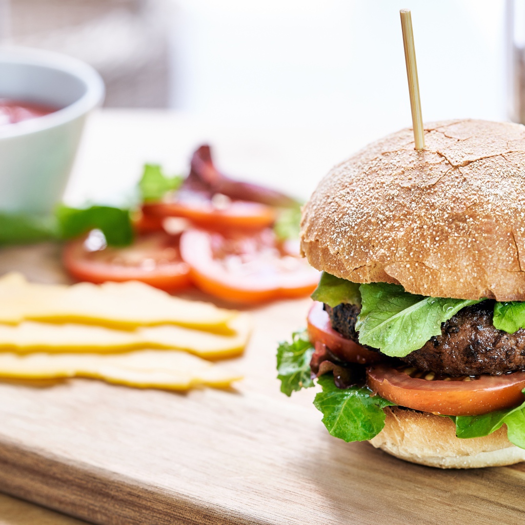 Аппетитный гамбургер на доске с сыром и помидорами