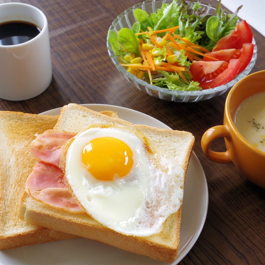 Тосты с яичницей и беконом на столе с салатом, кофе и супом