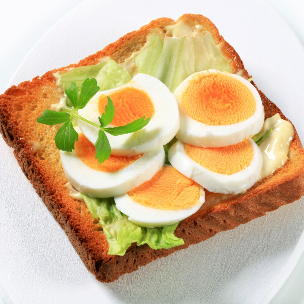 Тост с листом салата и кусочками яйца на белой тарелке 