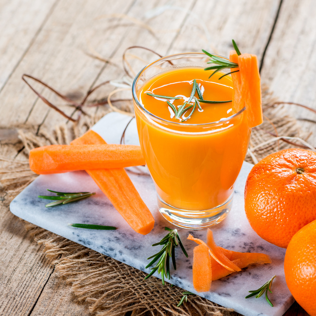 Два апельсина на столе со стаканом морковного сока