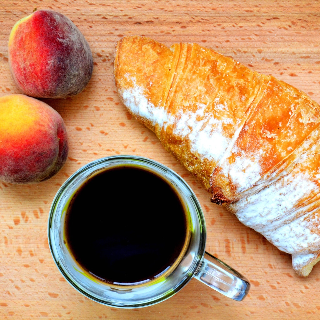 Два персика на столе с кофе и круассаном