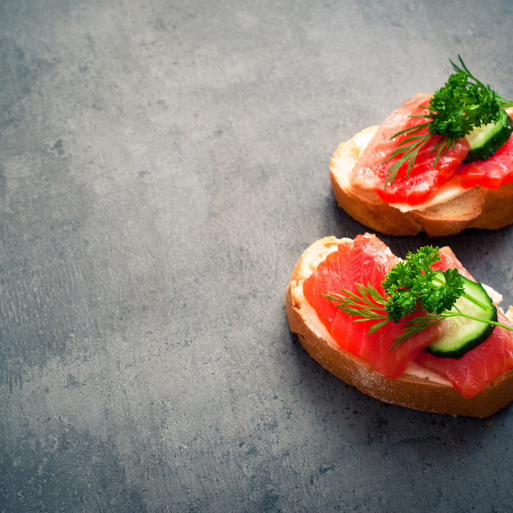 Два бутерброда с красной рыбой, огурцом и зеленью на черном фоне