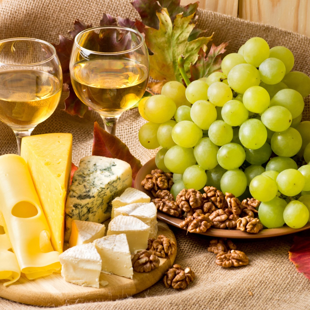 Белое вино на столе с сыром, виноградом и орехами