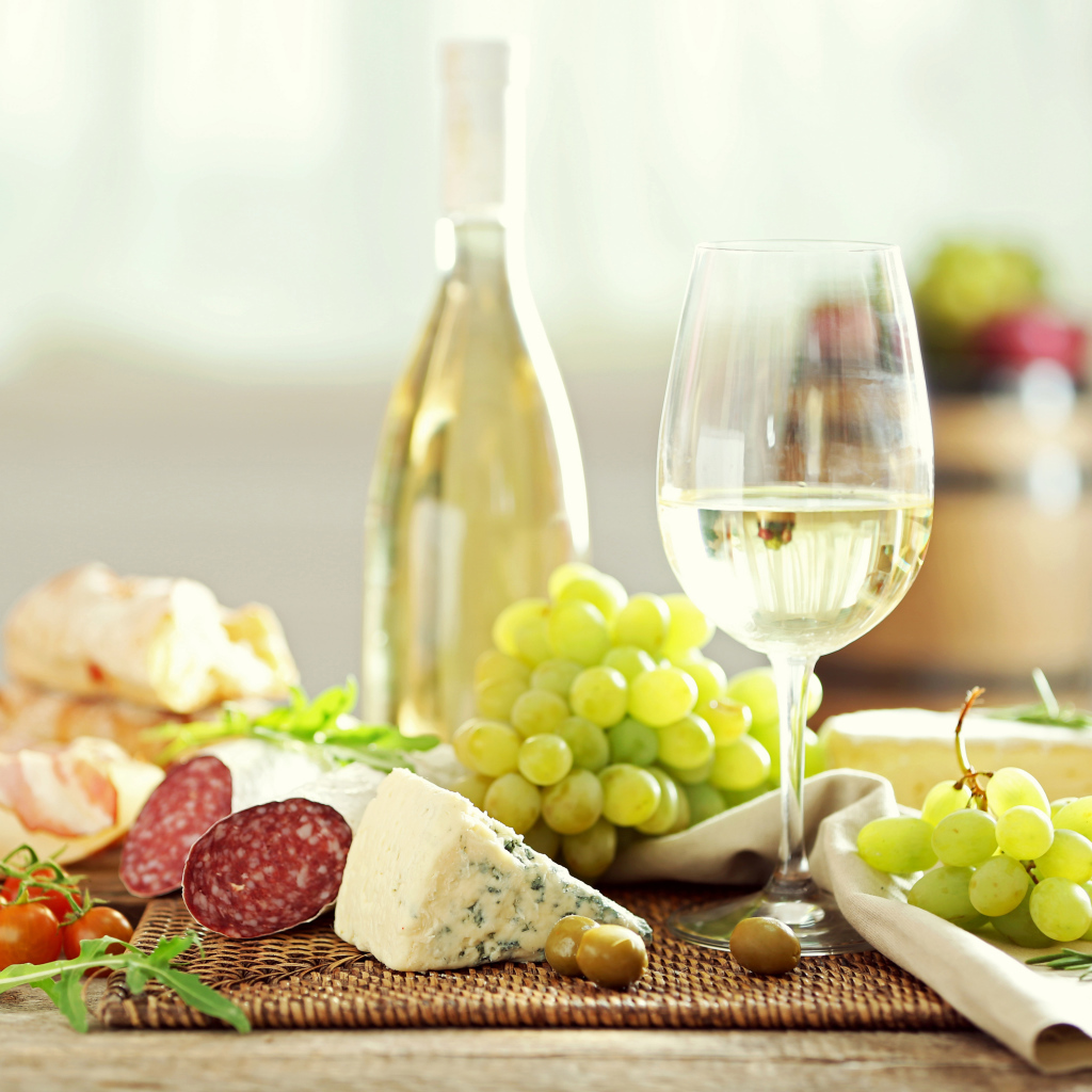 Белое вино на столе с сыром, колбасой и виноградом