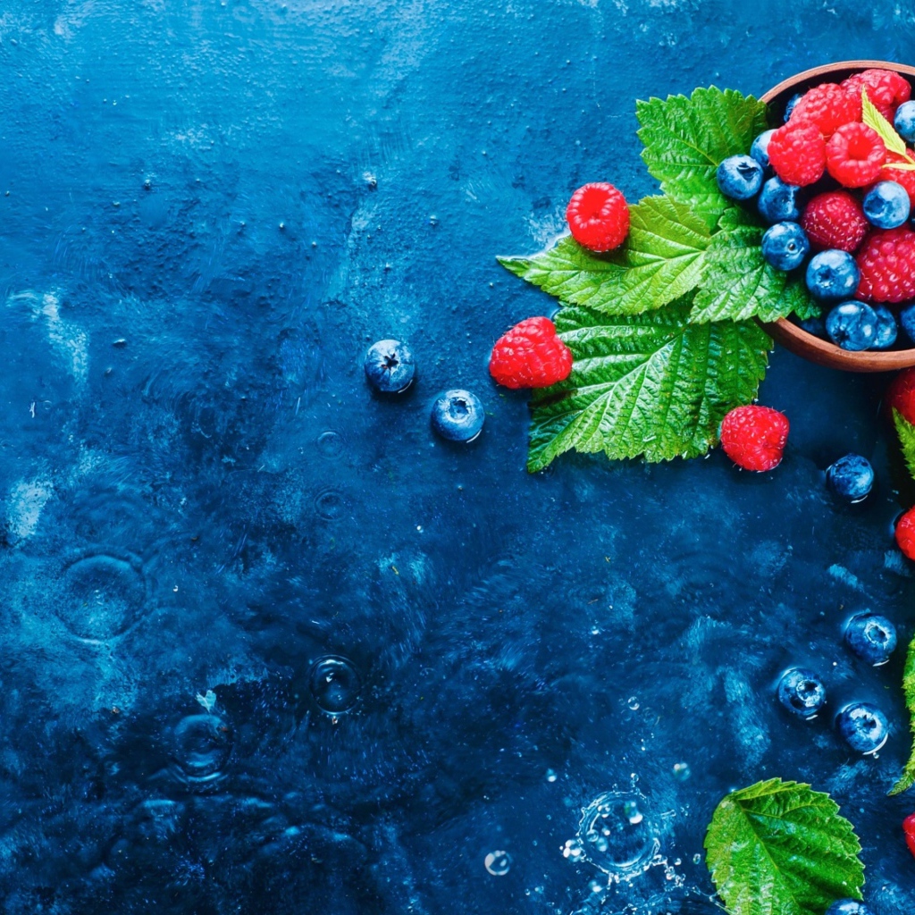Чашка с ягодами черники и малины на синем столе