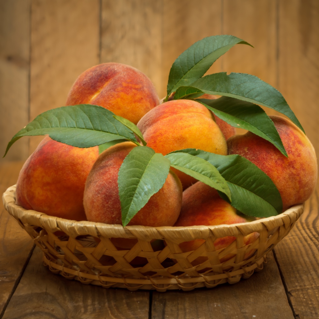 Корзинка персиков с зелеными листьями на столе
