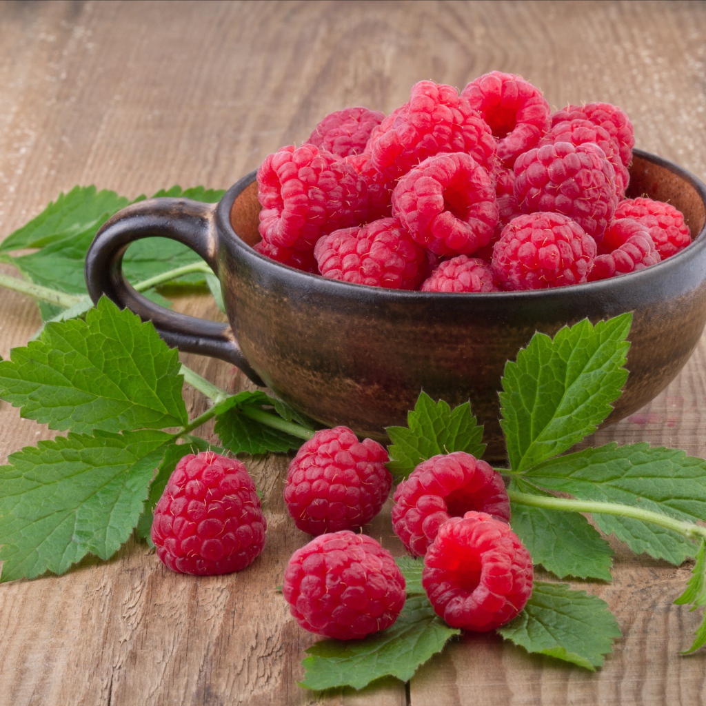 Чашка со свежей малиной на столе с зелеными листьями