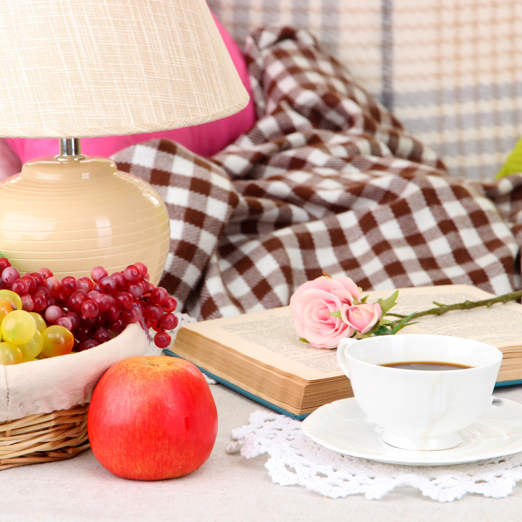 Фрукты в корзине на столе с книгой, чашкой кофе и розой