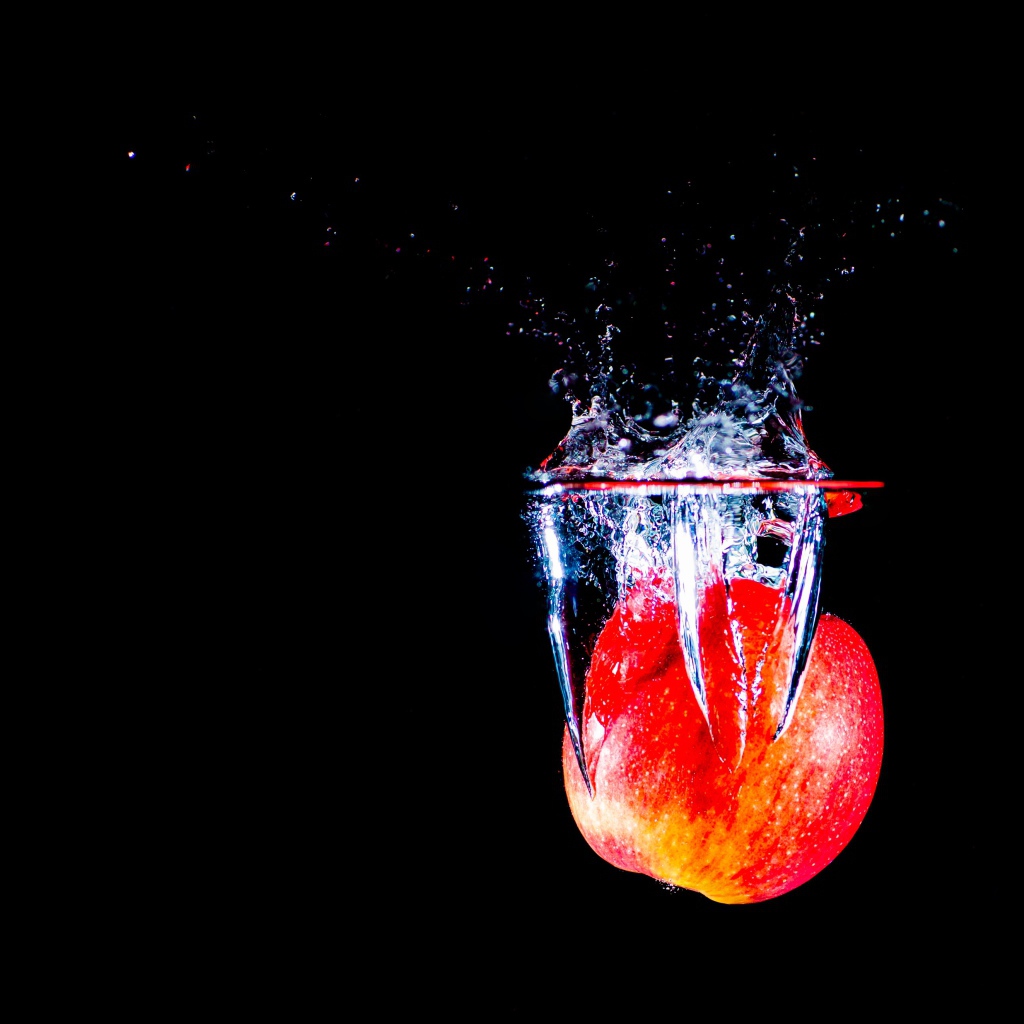 Красное яблоко падает в воду на черном фоне