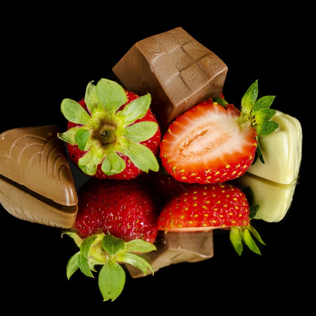 Красная свежая клубника с шоколадными конфетами на черном фоне