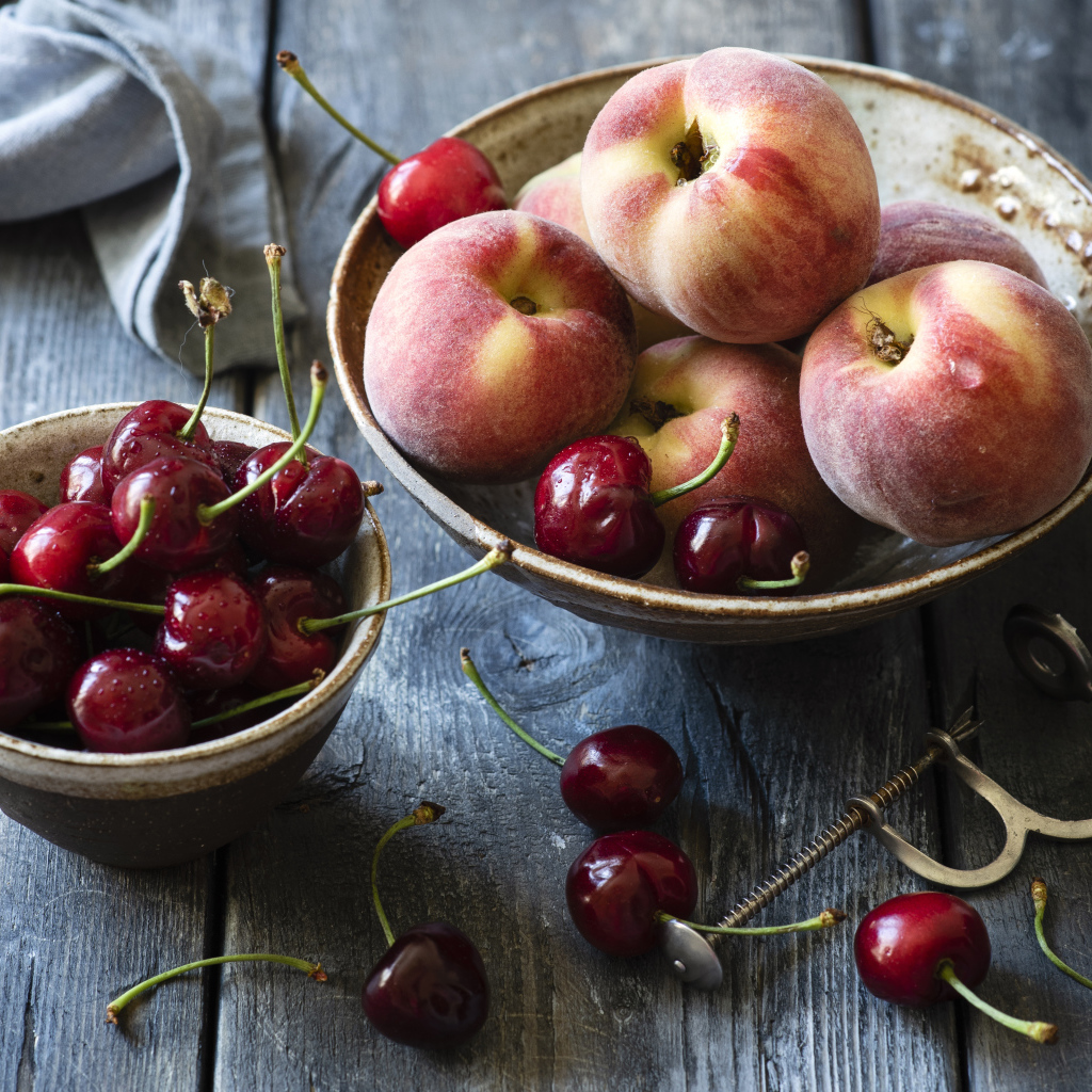 Спелые персики в миске на столе с черешней