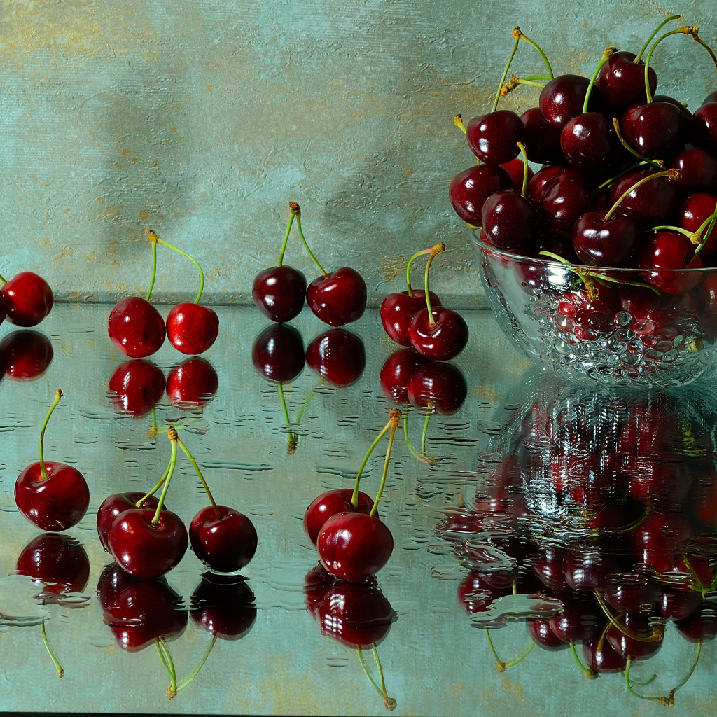 Спелые красные черешни отражаются в поверхности стола