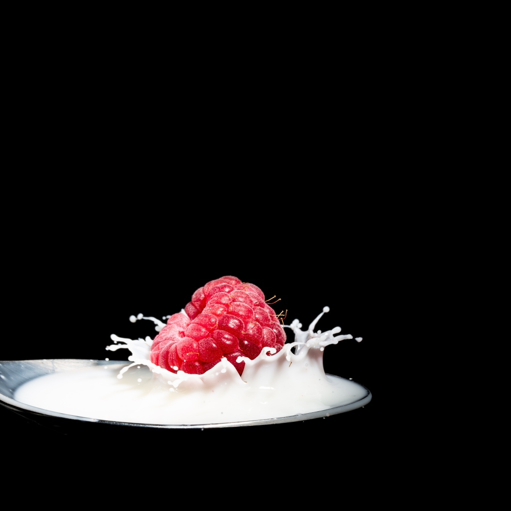 Спелая красная малина с ложке с молоком на черном фоне