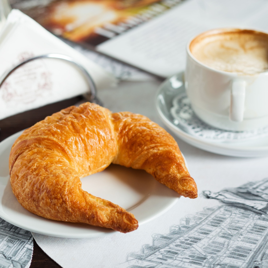 Круассан на белой тарелке с чашкой капучино 