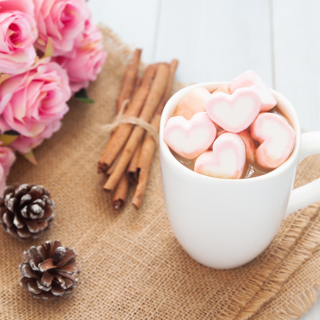 Чашка какао с маршмеллоу на столе с корицей, шишками и букетом розовых роз