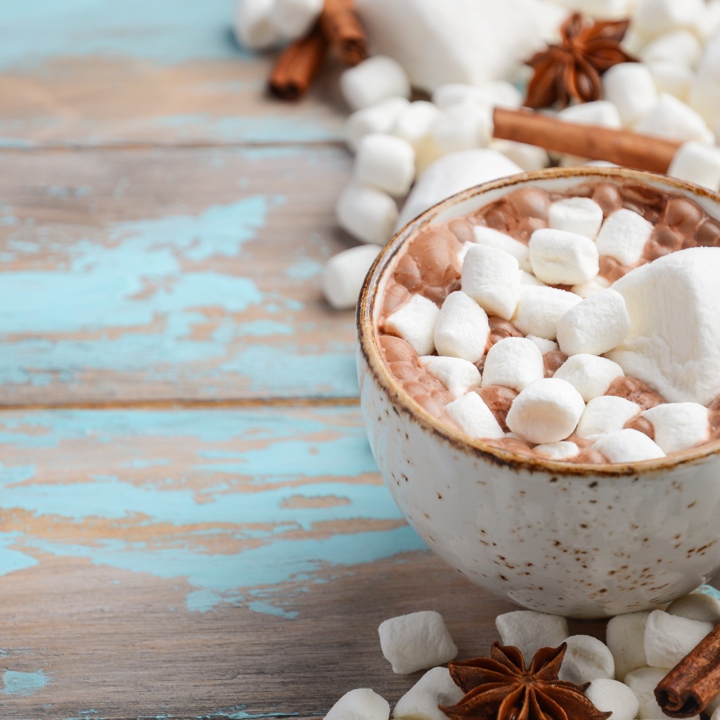 Чашка какао с маршмеллоу на столе с корицей и сладостями