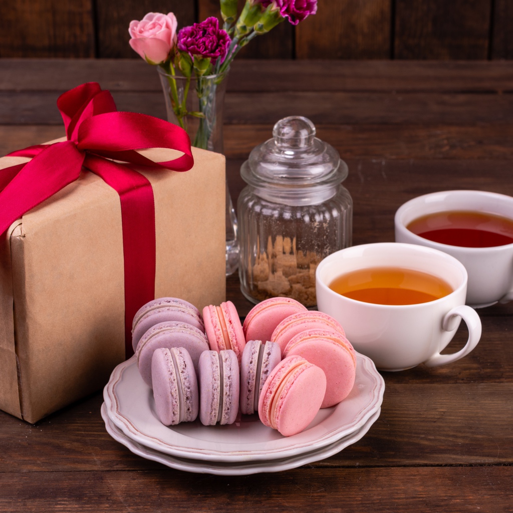 Подарок с красной лентой на столе с макарунами и чаем 