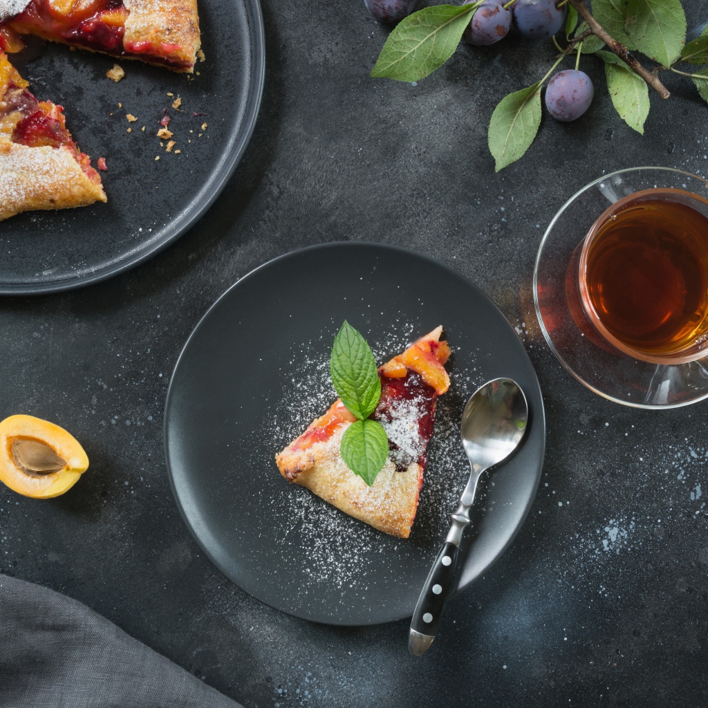 Кусок пирога с сахарной пудрой и абрикосами и сливами на столе с чаем 