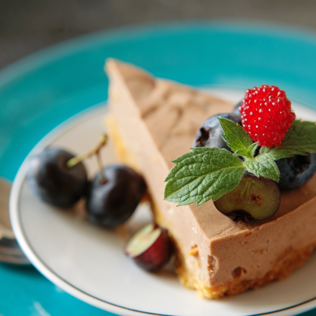 Кусок чизкейка на тарелке с ягодами черники и малиной