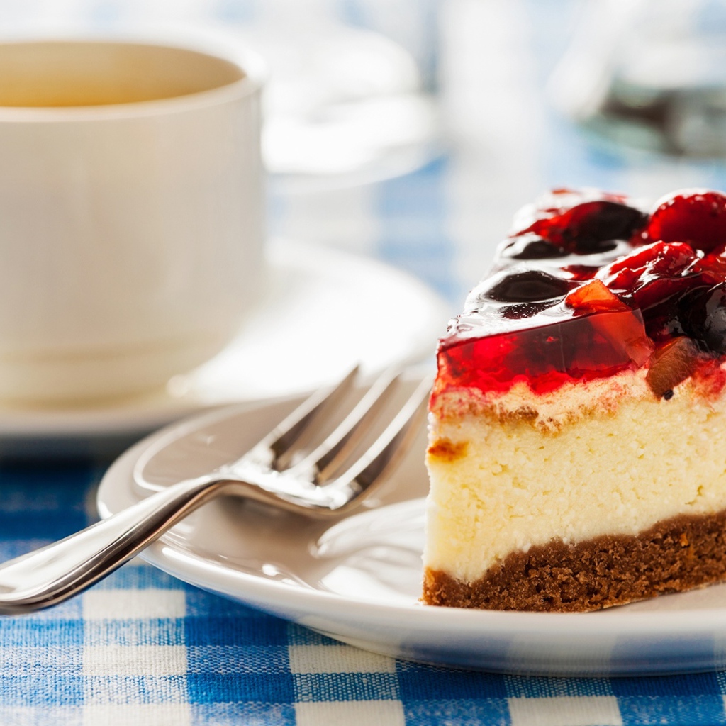 Кусок чизкейка с ягодами и желе на столе с чашкой кофе