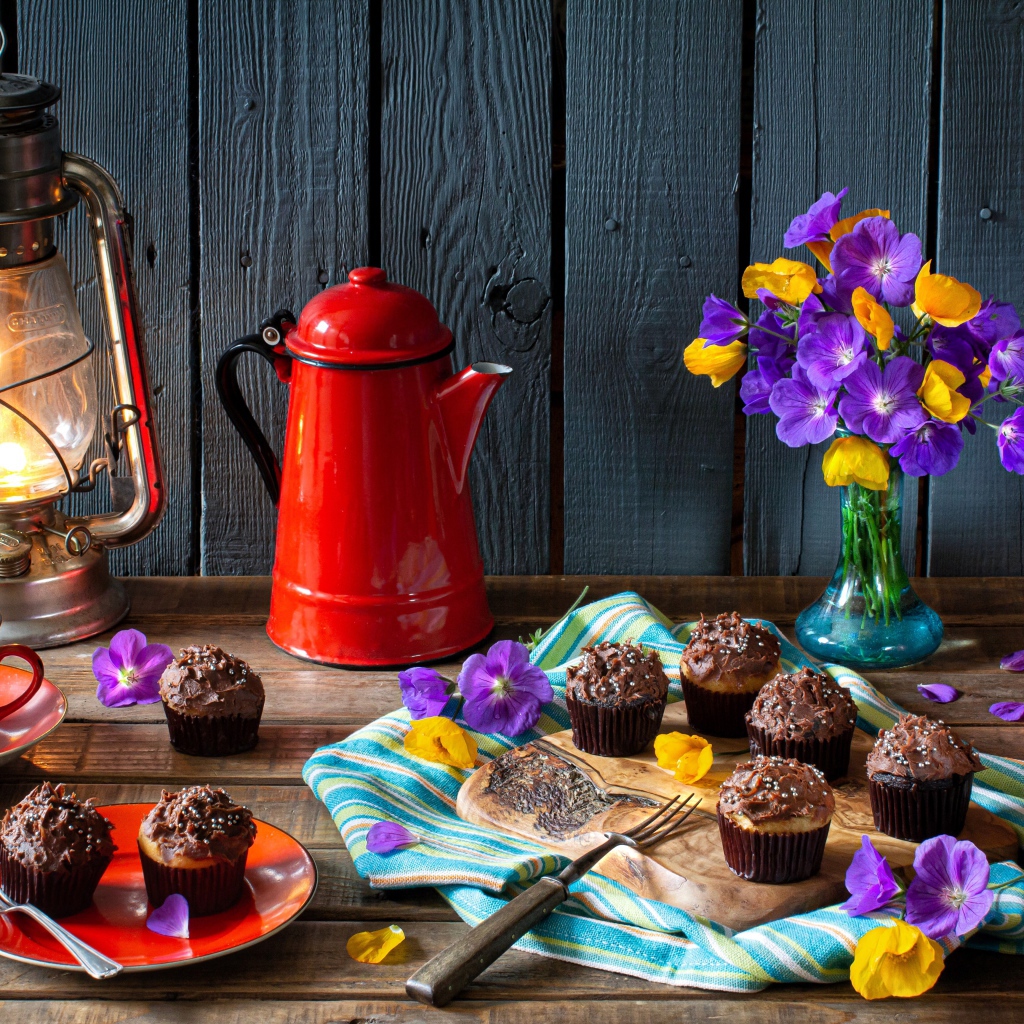 Аппетитные свежие кексы с кремом на столе с кофе, лампой и букетом цветов