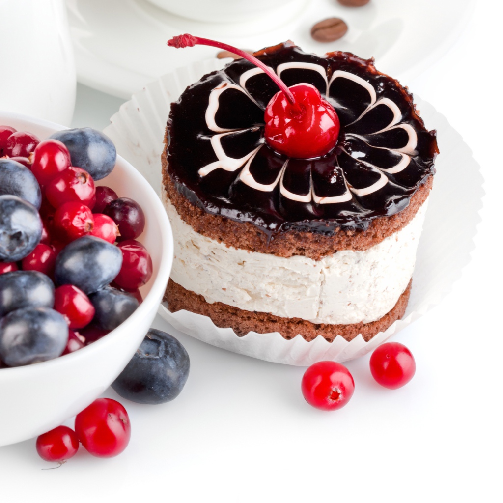 Пирожное с вишней на белом фоне с ягодами черники и клюквы