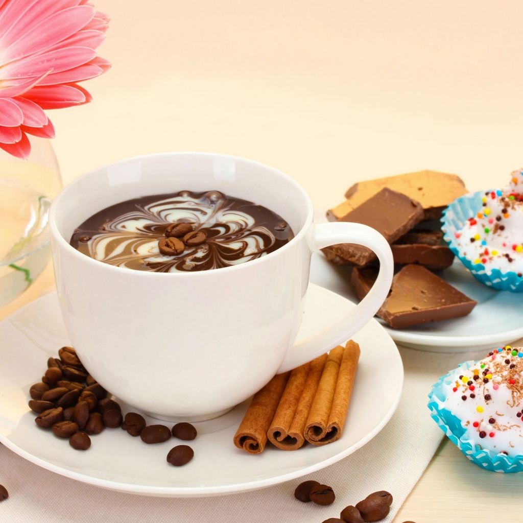 Конфеты на столе с кофе и герберой в вазе 