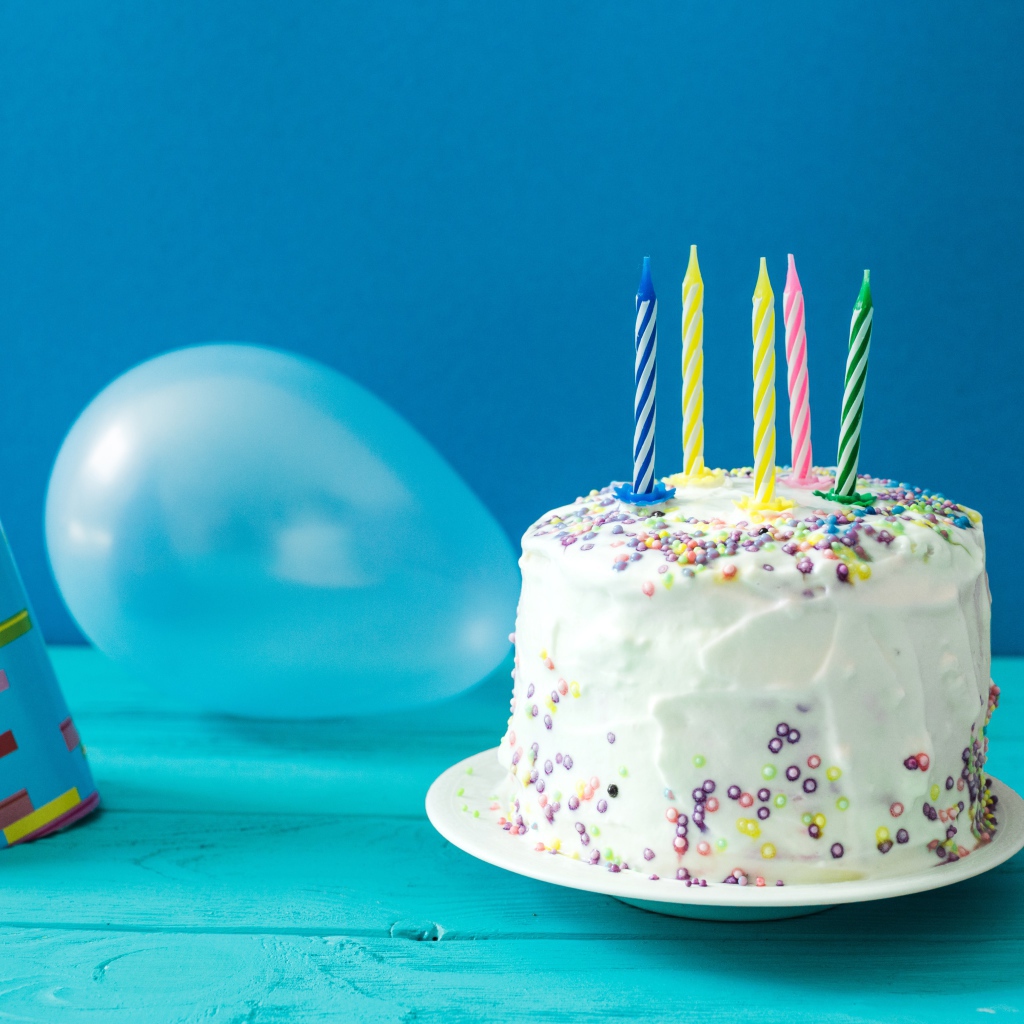 Праздничный торт со свечами, шариком и колпаком на голубом фоне