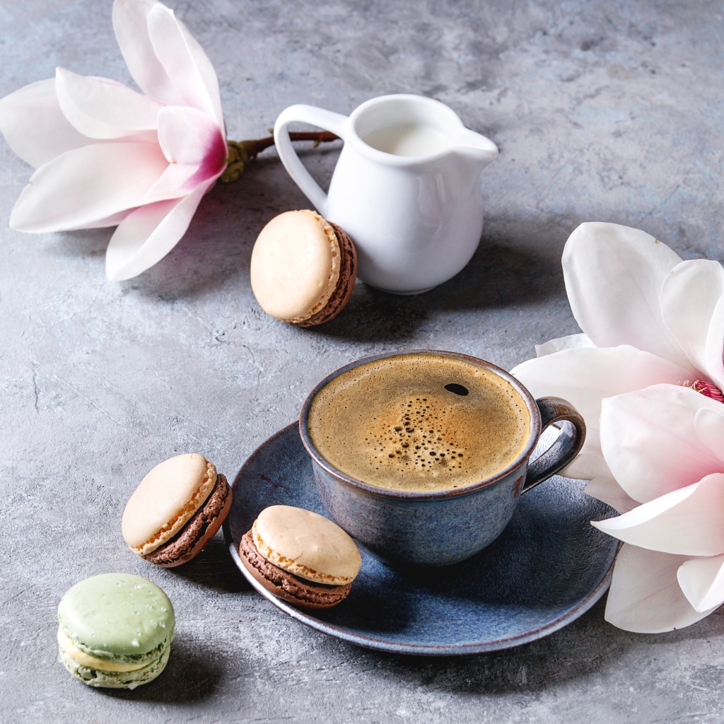 Кофе на столе с макарунами, молоком и цветами 