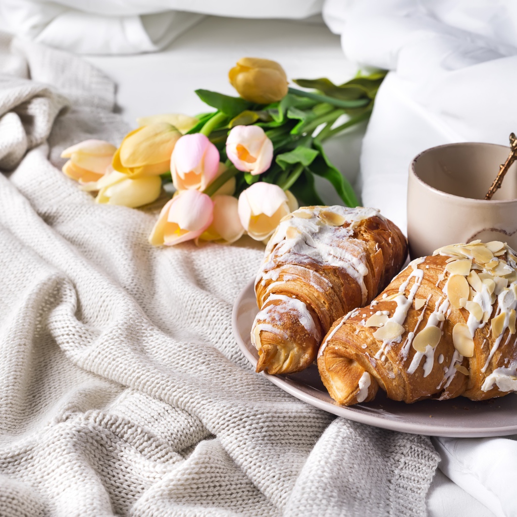Круассаны на кровати с кофе и букетом тюльпанов