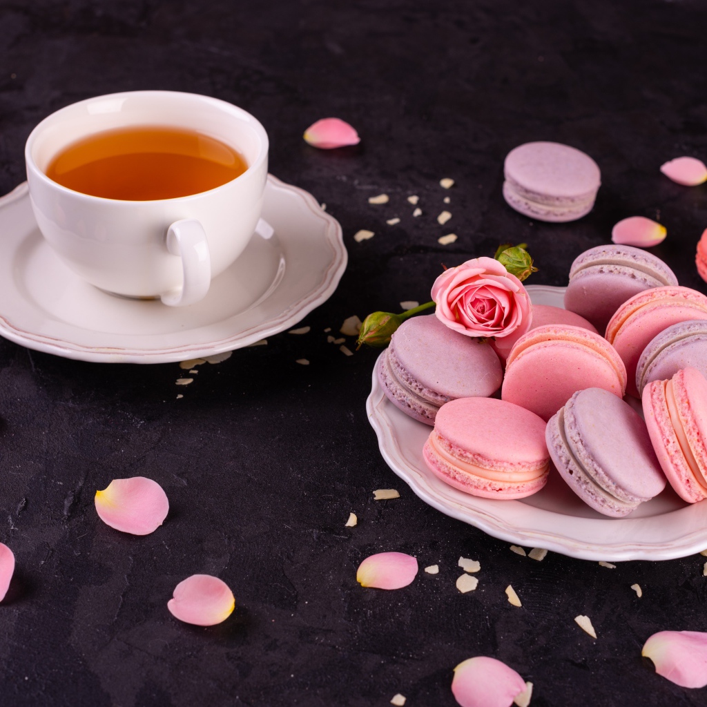 Нежный десерт макарон на столе с чашкой чая и розой
