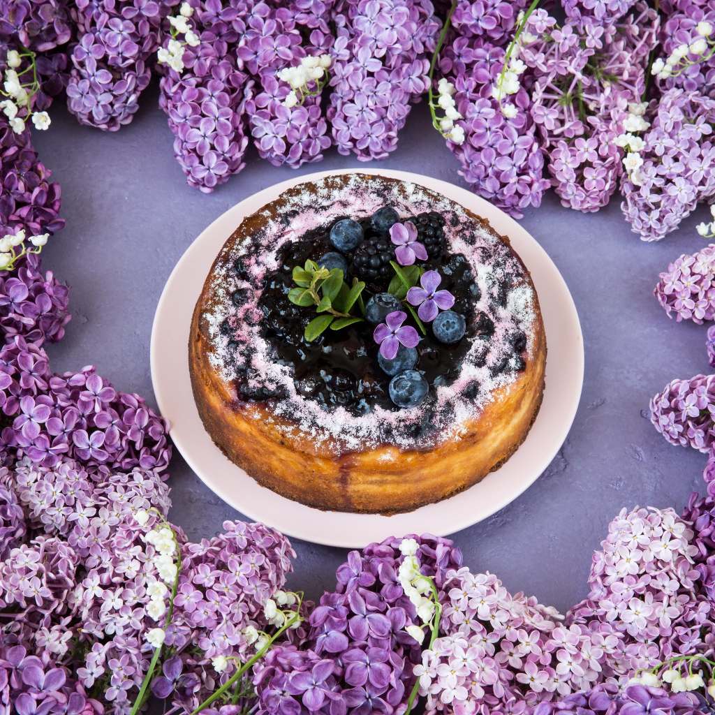 Аппетитный пирог с ягодами на столе с цветами сирени