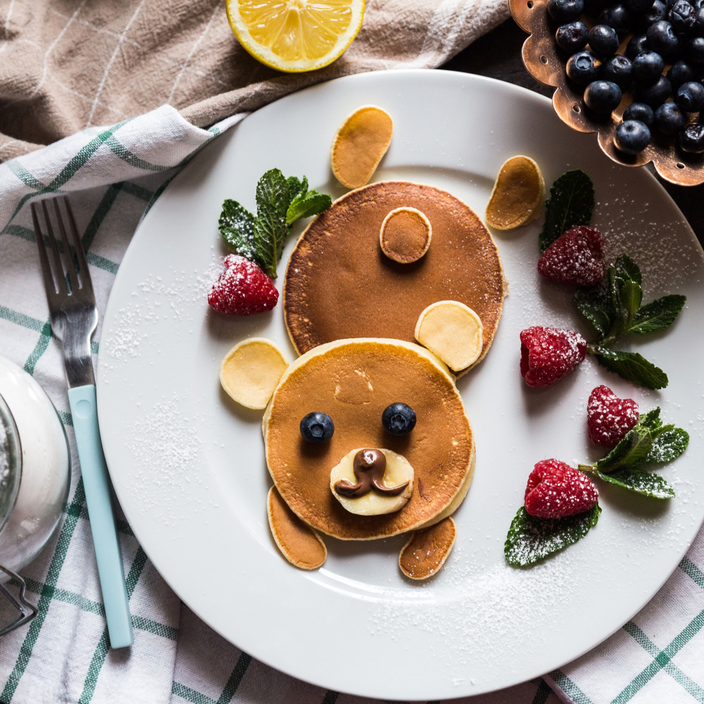 Медведь из оладьев на тарелке с малиной и сахарной пудрой