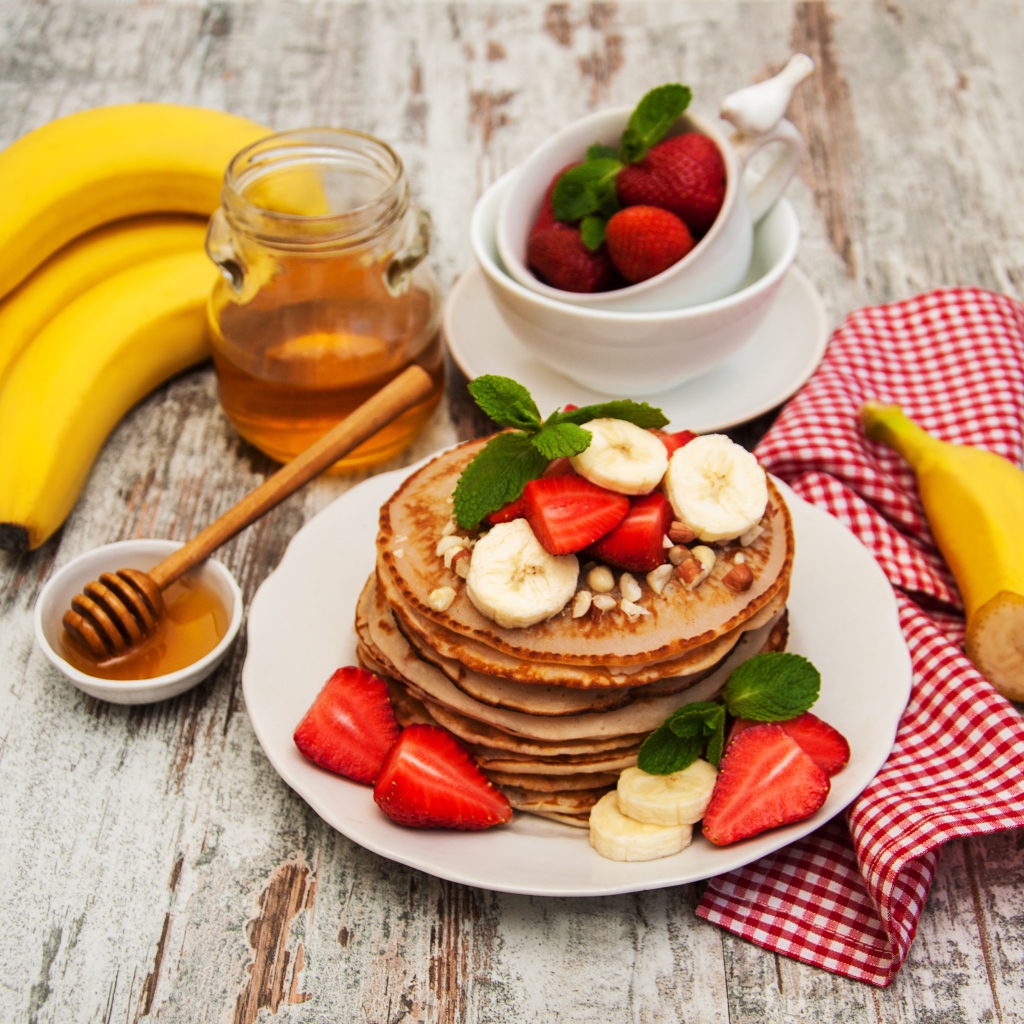 Оладьи с бананами и клубникой на столе с медом
