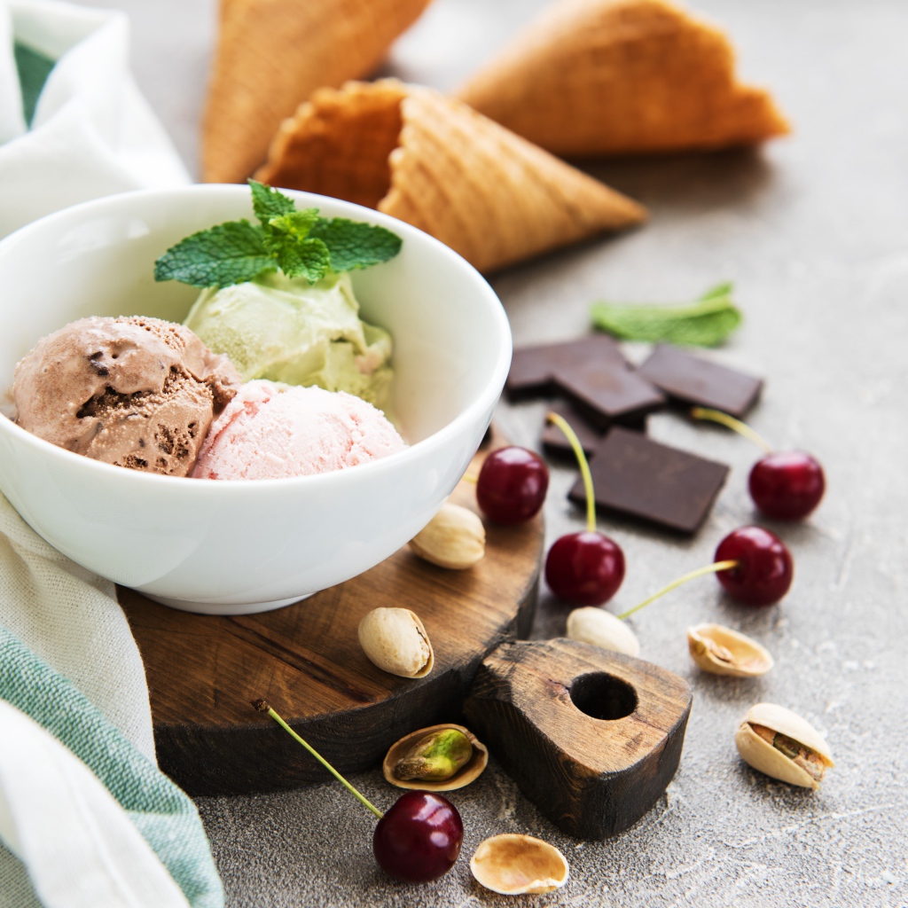 Шарики мороженого на столе вафельными рожками, черешней и фисташками