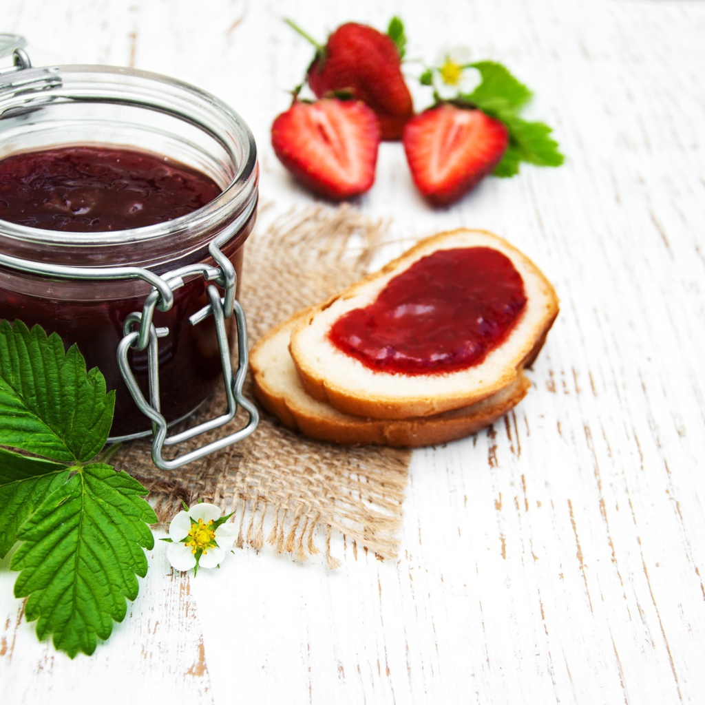 Банка клубничного джема на столе с батоном