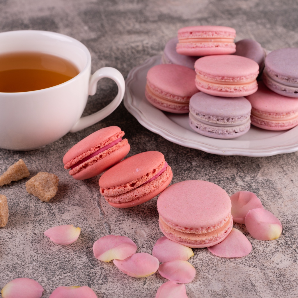 Сладкий десерт макарун на столе с чашкой чая, сахаром и лепестками розы