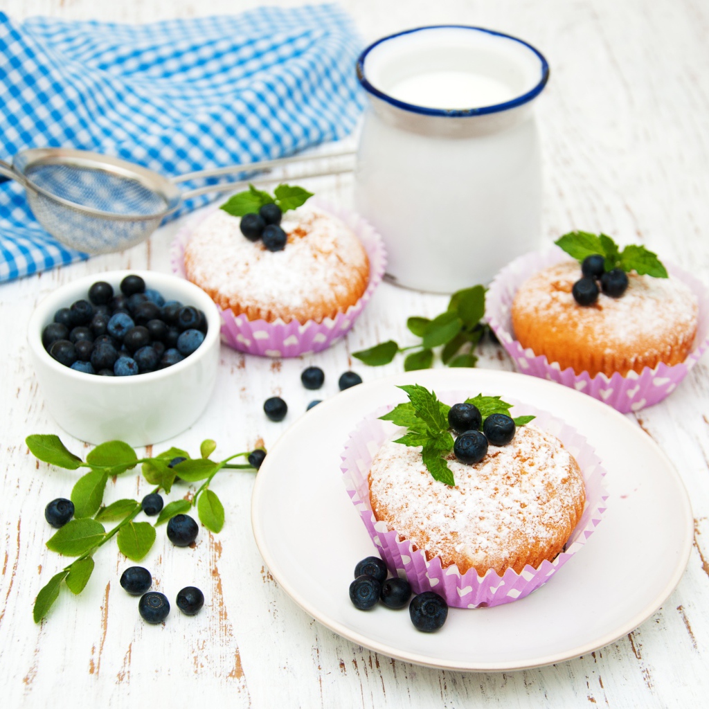 Кексы с сахарной пудрой на столе с молоком и черникой